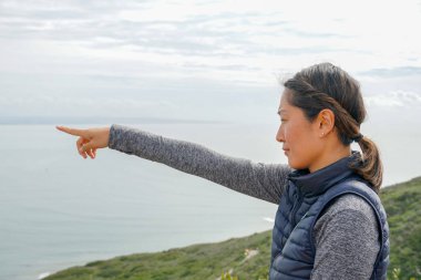 Genç sporcu Asyalı kadın güzel okyanus manzarasına bakıyor. Yürüyüş yapan genç bir kadın manzaraya hayran. sağlıklı aktif yaşam biçimi.