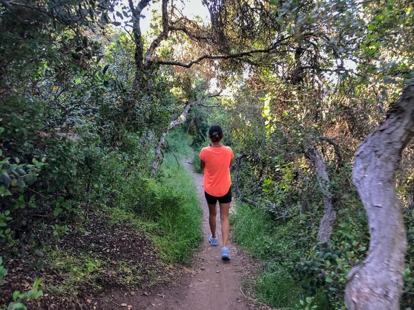 Young athletic sporty girl with long hair in pink sleeveless shirt training running in green mountain forest during summer season. San Diego, California, USA