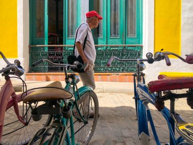 Eski Havana, Küba merkezinde park edilmiş farklı eski tarz renkli bisiklet ile sokakta yürüyen yaşlı Kübalı adam. Bisiklet Havana tarihi eski bölümünde park. Küba.