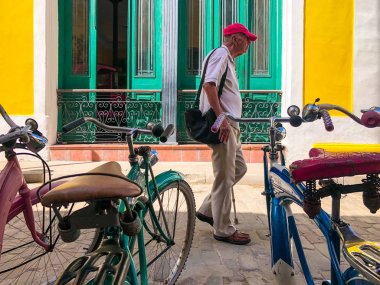 Eski Havana, Küba merkezinde park edilmiş farklı eski tarz renkli bisiklet ile sokakta yürüyen yaşlı Kübalı adam. Bisiklet Havana tarihi eski bölümünde park. Küba.