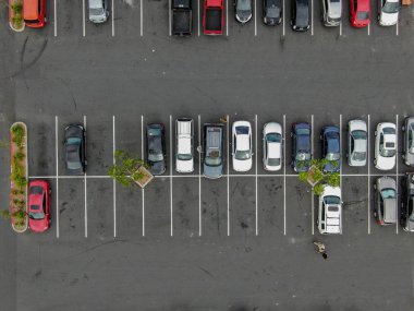 Renkli araç çeşitleri ile süpermarkette otopark havadan üst görünümü. İnsanlar arabalarına yürüyüp park etmeye çalışıyor..