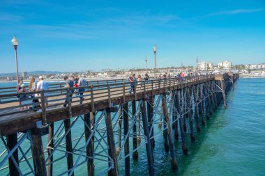 Mavi yaz gününde Oceanside İskelesi'nde yürüyen turist, Oceanside, kuzey San Diego County, Kaliforniya. Batı Amerika Birleşik Devletleri kıyı şeridinde ahşap iskele. Balıkçı ile ünlüdür. 