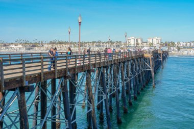 Mavi yaz gününde Oceanside İskelesi'nde yürüyen turist, Oceanside, kuzey San Diego County, Kaliforniya. Batı Amerika Birleşik Devletleri kıyı şeridinde ahşap iskele. Balıkçı ile ünlüdür. 