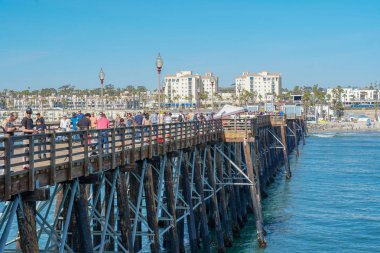 Mavi yaz gününde Oceanside İskelesi'nde yürüyen turist, Oceanside, kuzey San Diego County, Kaliforniya. Batı Amerika Birleşik Devletleri kıyı şeridinde ahşap iskele. Balıkçı ile ünlüdür. 