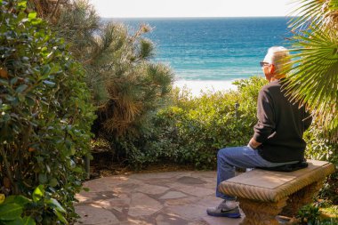 Güneşli bir gün boyunca güzel deniz manzarası düşünen bir uçurumda denizin üstünde bir kaya bankta oturan yaşlı adam. San Diego, Kaliforniya, ABD. 
