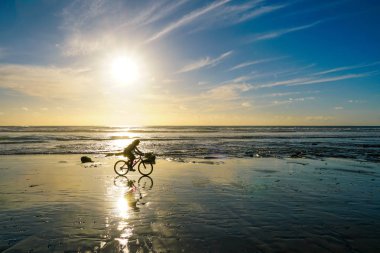Gün batımı huzurlu an sırasında plajda zevk ve bisiklet insanların silüeti. Alacakaranlık zaman ve deniz üzerinde yansıma güzel gökyüzü.