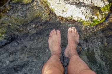 Bir dağ nehrinin küçük kayalarıyla berrak suya daldırılalı ayaklar.