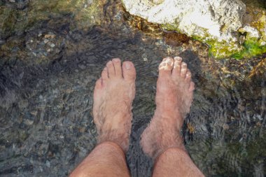 Bir dağ nehrinin küçük kayalarıyla berrak suya daldırılalı ayaklar.