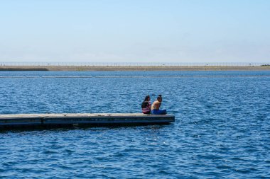 Arkadaşlar mutluluk. Yong kızlar ahşap iskelede oturan ve bir dinlenme zaman yaşıyorsanız. Miramare Gölü, San Diego, Kaliforniya, Amerika Birleşik Devletleri.