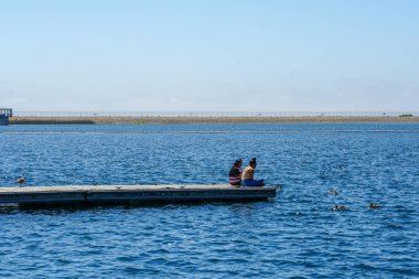 Arkadaşlar mutluluk. Yong kızlar ahşap iskelede oturan ve bir dinlenme zaman yaşıyorsanız. Miramare Gölü, San Diego, Kaliforniya, Amerika Birleşik Devletleri.