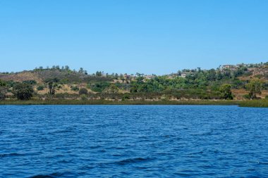 Güzel mavi gökyüzü yaz gününde mavi su, ağaçlar ve yerli sulak bitkiler ile büyük rezervuar gölü. Scripps Miramar Ranch topluluğunda Miramar rezervuarı, San Diego, Kaliforniya. 