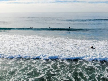 La Jolla, San Diego, California, Abd'de güzel mavi suda bekleyen, kürek çeken ve dalgaların tadını çıkaran sörfçülerin havadan görünümü.