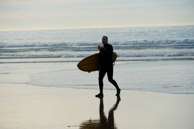 La Jolla Beach, San Diego, California, Abd' de, gün batımı saatinde sahilde sörf tahtası tutan ıslak takım elbiseli sörfçü. 