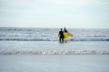 Islä±k elbiseli sörf Ã§ift sahilde sarÄ± sörf tahtasÄ±nÄ± tutarken. Sörfçü ler suya gidiyor, La Jolla State Beach, Kaliforniya, San Diego County bulunan. Abd