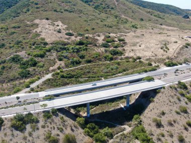 Yol köprüsünün havadan görünüşü, vadideki viyadük destekleri kuru sarı tepelerin arasında.