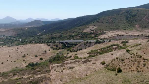 Вид с воздуха на автодорожный мост, опоры виадука в долине среди сухих желтоватых холмов — стоковое видео