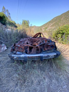 Mavi gökyüzüne karşı dağda terk edilmiş bir araba.