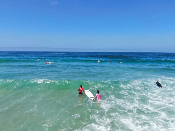 Вид с воздуха на серферов, ждущих и гребущих к волнам в голубой воде — стоковое фото