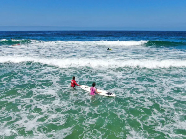 Vista aérea de surfistas esperando y remando a las olas en agua azul —  Fotos de Stock