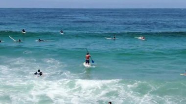 Sörfçülerin mavi sudaki dalgalara doğru kürek çekişlerini gösteren hava manzarası.