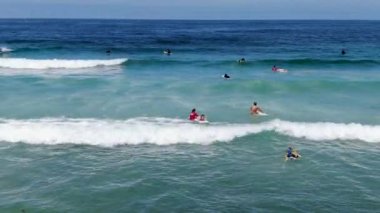 Sörfçülerin mavi sudaki dalgalara doğru kürek çekişlerini gösteren hava manzarası.