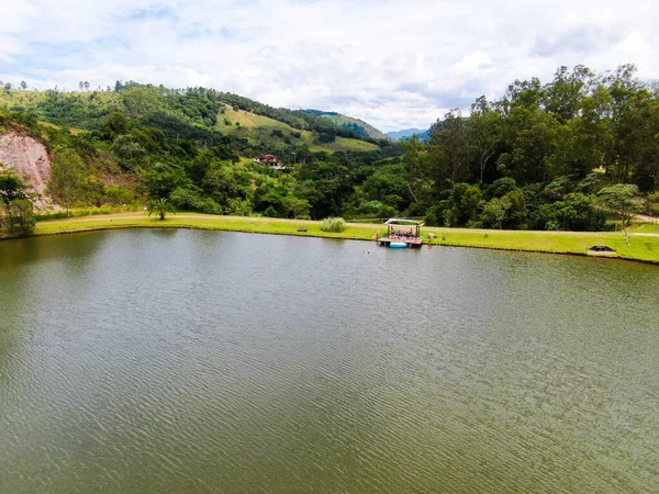 Vista aérea da pequena cabana de madeira ao lado do lago no vale, com a família desfrutando de relaxar momento — Fotografia de Stock