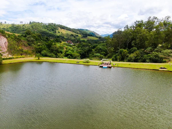 Vista aérea da pequena cabana de madeira ao lado do lago no vale, com a família desfrutando de relaxar momento — Fotografia de Stock