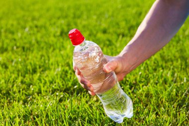 Saf su bir şişe yeşil bulanık çim arka planda tutan el