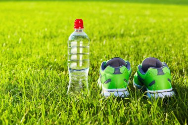 Spor ayakkabı spor ayakkabı ve şişe suyu taze yeşil çimenlerin üzerinde. Spor donatımı. Açık havada spor. Metin için yer