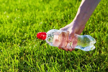 Saf su bir şişe yeşil bulanık çim arka planda tutan el