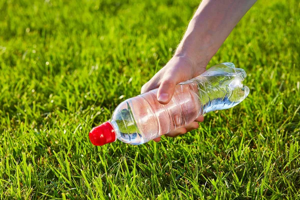 Hand holding a bottle of pure water against green blurred grass background