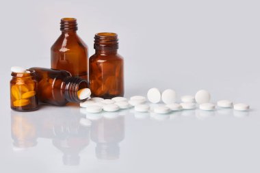 Tabletler ve hapları beyaz ayna arka plan üzerinde beyaz. Sağlık kavramı. Cam kahverengi şişe dağınık takviyeleri