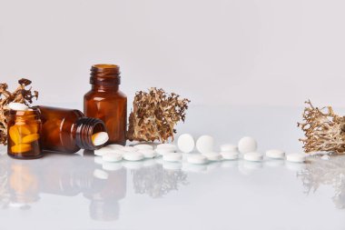 Tabletler ve ilaçlarla liken (Cetraria islandica) beyaz ayna arka plan üzerinde beyaz. Sağlık kavramı, öksürük ilacı. Homeopatik kavramı. Cam kahverengi şişe dağınık takviyeleri  