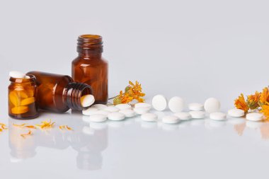 Tabletler ve hapları ile kadife çiçeği (Calendula) beyaz ayna arka plan üzerinde beyaz. Sağlık kavramı. Homeopatik kavramı. Cam kahverengi şişe dağınık takviyeleri  