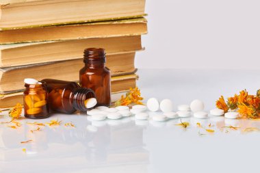 Tabletler ve hapları kadife çiçeği (Calendula) ve eski kitaplar beyaz ayna arka plan üzerinde beyaz. Sağlık kavramı. Homeopatik kavramı. Cam kahverengi şişe dağınık takviyeleri  