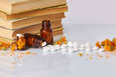 Tabletler ve hapları kadife çiçeği (Calendula) ve eski kitaplar beyaz ayna arka plan üzerinde beyaz. Sağlık kavramı. Homeopatik kavramı. Cam kahverengi şişe dağınık takviyeleri  