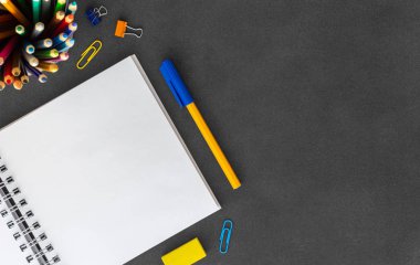 Kalem, renkli kalemler, silgi, kağıt küme, boş koyu arka plan üst görünüm üzerinde ataş ile açık beyaz boş spiral kağıt defter