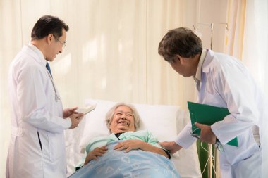 Genç doktor ve Yardımcısı bir tedavi kadın kıdemli hasta için hasta yatağının içinde var,