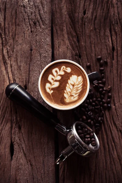 Sıcak latte kahve siyah Kupası ve kahve demlemek tutucu kahve çekirdekleri ile yıpranmış ahşap masa üzerinde