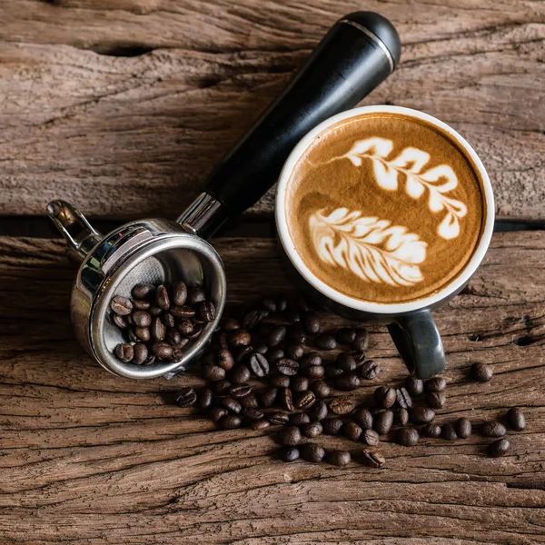 热拿铁咖啡在黑色杯子和咖啡酿造持有人在风化木桌与咖啡豆 — 图库照片