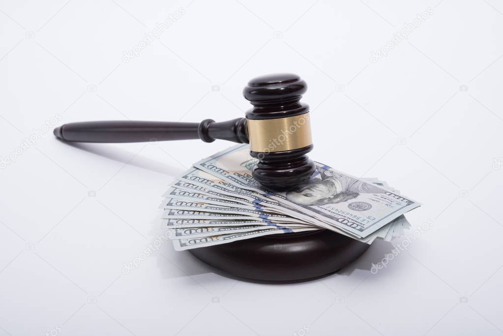 Wooden auctioneer or judges gavel for dispensing justice or knocking down sale prices  on pile of US dollars agains white background