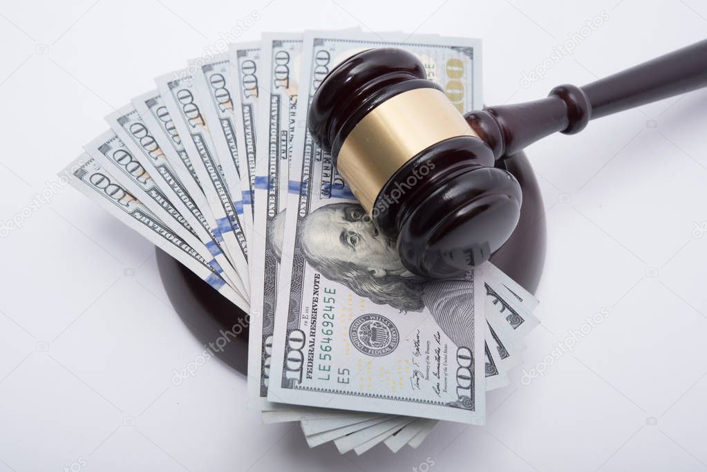 Wooden auctioneer or judges gavel for dispensing justice or knocking down sale prices  on pile of US dollars agains white background