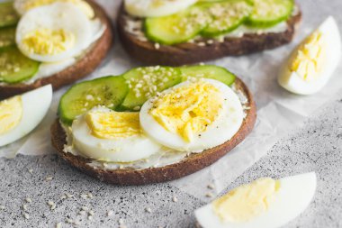 Yumurtalı sandviç, salatalık, susam tohumu ve baharat. Lezzetli bir kahvaltı. Sandviçler masada.