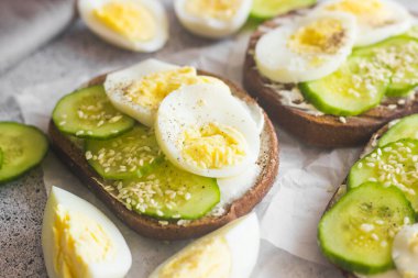 Yumurtalı sandviç, salatalık, susam tohumu ve baharat. Lezzetli bir kahvaltı. Sandviçler masada.