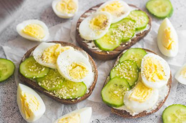 Yumurtalı sandviç, salatalık, susam tohumu ve baharat. Lezzetli bir kahvaltı. Sandviçler masada.
