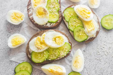 Yumurtalı sandviç, salatalık, susam tohumu ve baharat. Lezzetli bir kahvaltı. Sandviçler masada.