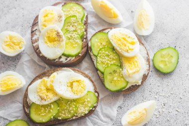 Yumurtalı sandviç, salatalık, susam tohumu ve baharat. Lezzetli bir kahvaltı. Sandviçler masada.
