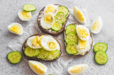 Yumurtalı sandviç, salatalık, susam tohumu ve baharat. Lezzetli bir kahvaltı. Sandviçler masada.