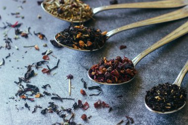 Kaşıklar içinde çeşitli bitki çayları. Çay yapraklı kaşıklar. Beton zeminde çay