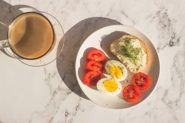 Masada nefis bir kahvaltı. Haşlanmış yumurta, domates, krem peynirli sandviç, tabakta dereotu.